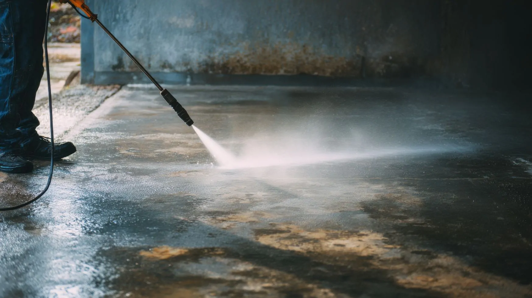 Man using hot water power washing to deep clean a garage floor Man using hot water power washing to deep clean a garage floor