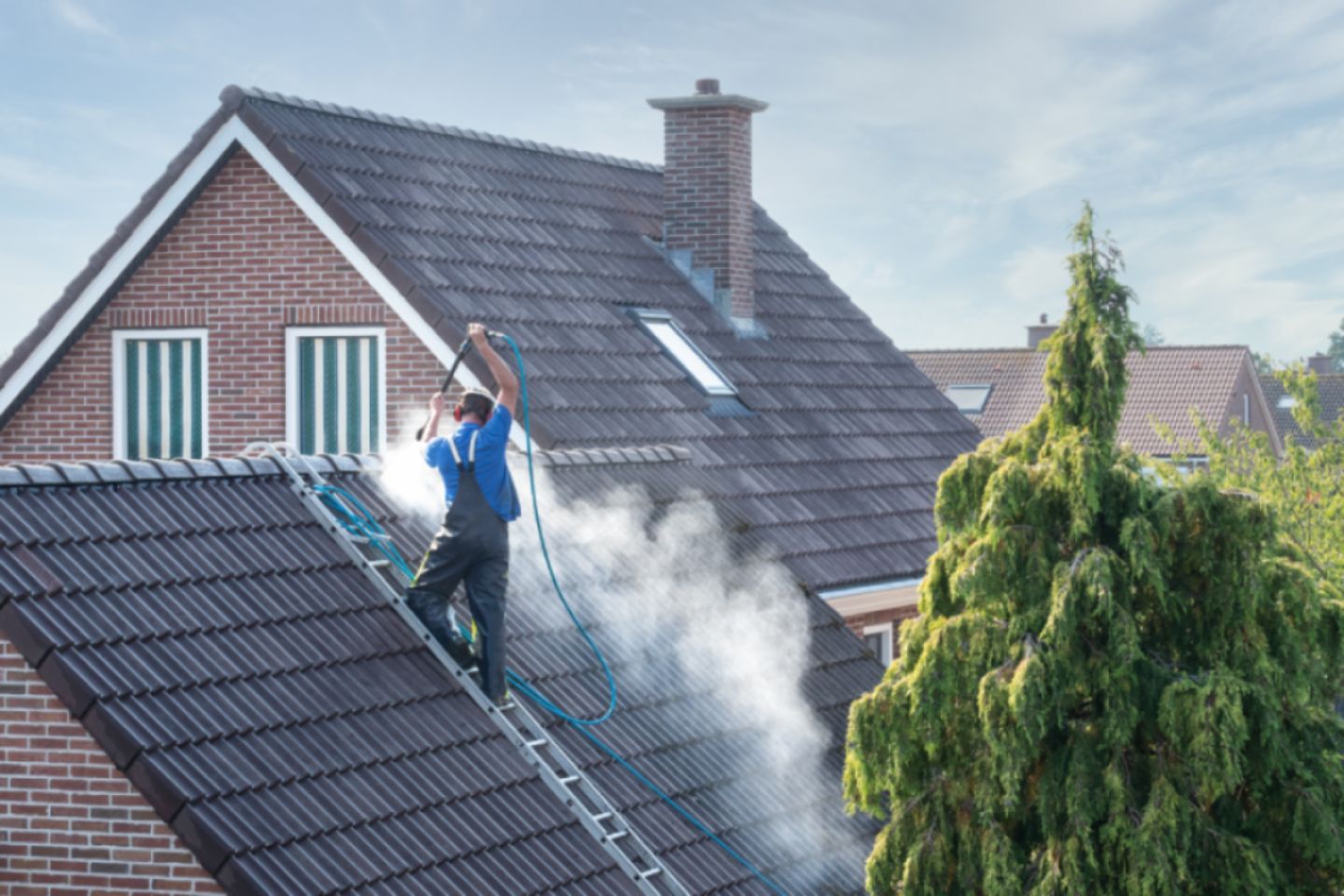 Cleaner using hot water power washing to clean a house roof