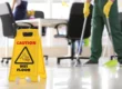 Wet floor caution sign in the foreground while a janitor mops during summer office cleaning in Arizona