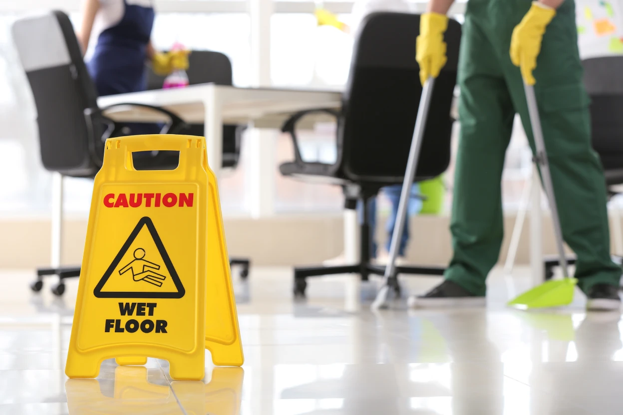 Wet floor caution sign in the foreground while a janitor mops during summer office cleaning in Arizona